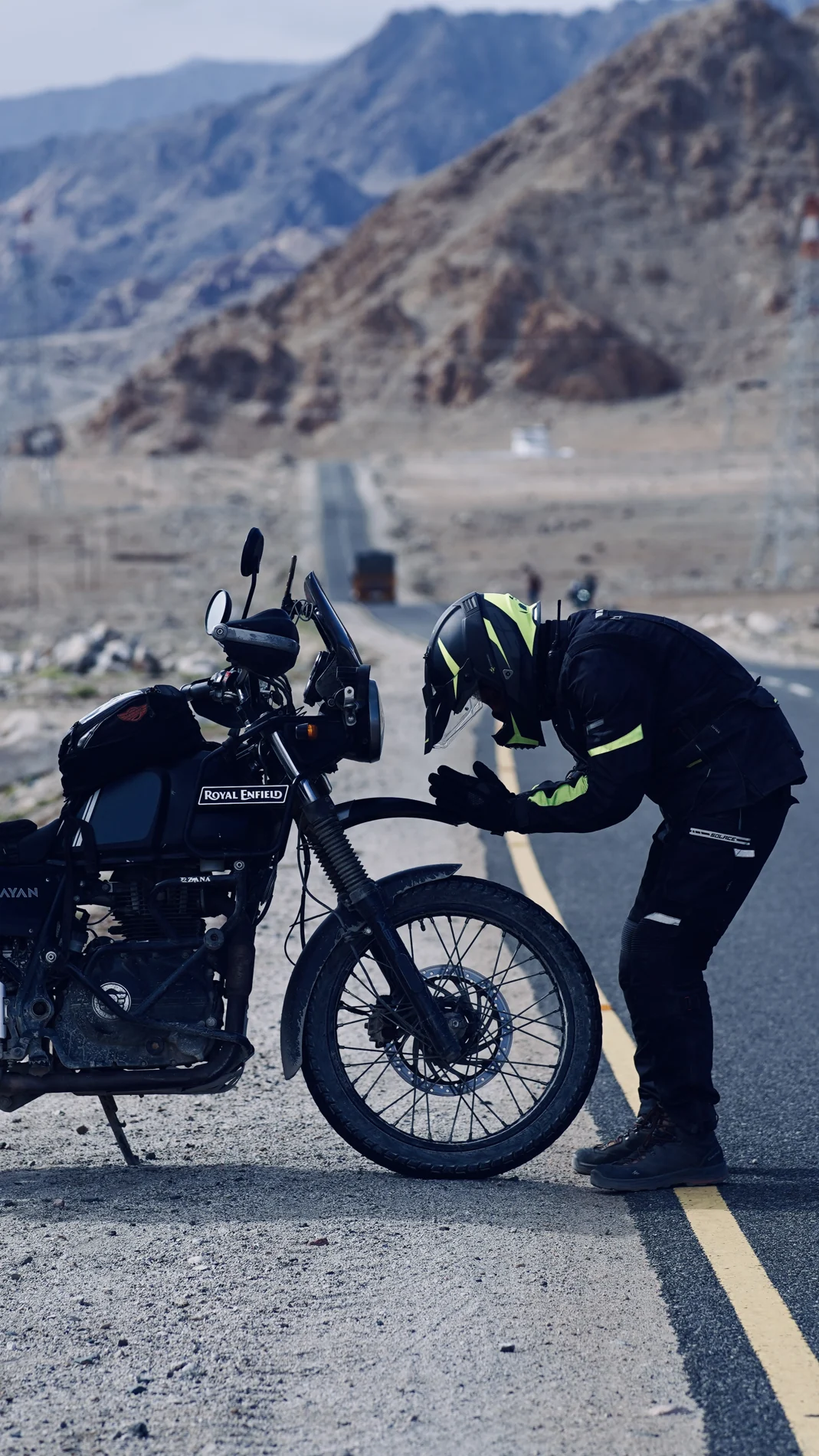 A rider beside a motorcycle on a mountain road